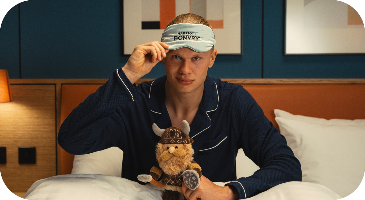 Soccer player Erling Haaland wearing a Marriott Bonvoy eye mask and holding a plush Viking toy.