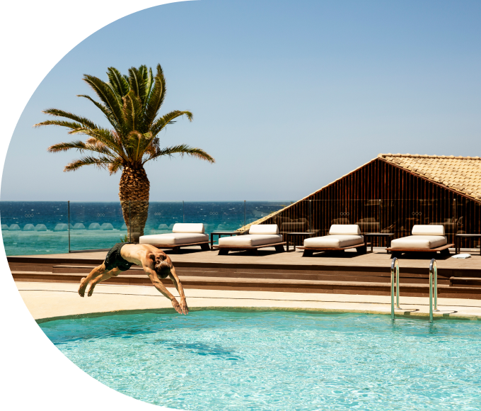 A guest diving into a pool at a tropical resort by the ocean.