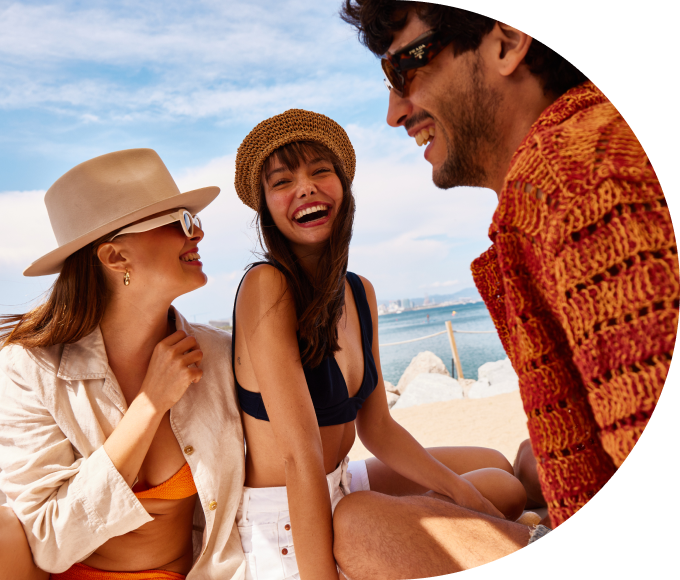 Three smiling guests sitting on a sunny, sandy beach.