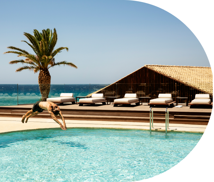 A guest diving into a pool at a tropical resort by the ocean.