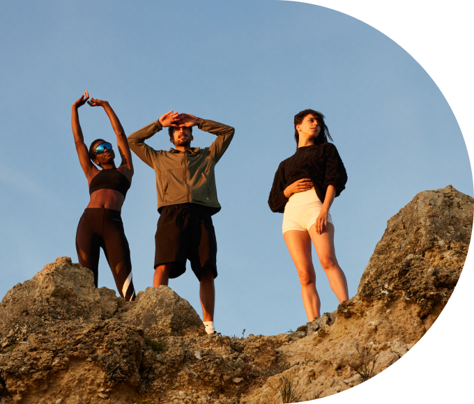 Three guests in athletic wear standing on a rocky peak against a clear blue sky.
