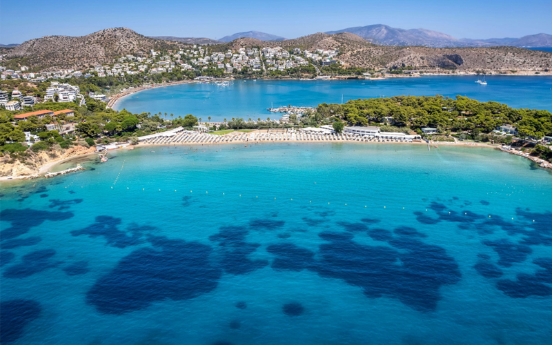 Overhead view of the Athenian Riviera, with clear blue waters and lush coastline. 