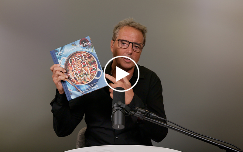 Dan Buettner holds his new cookbook in front of a microphone.
