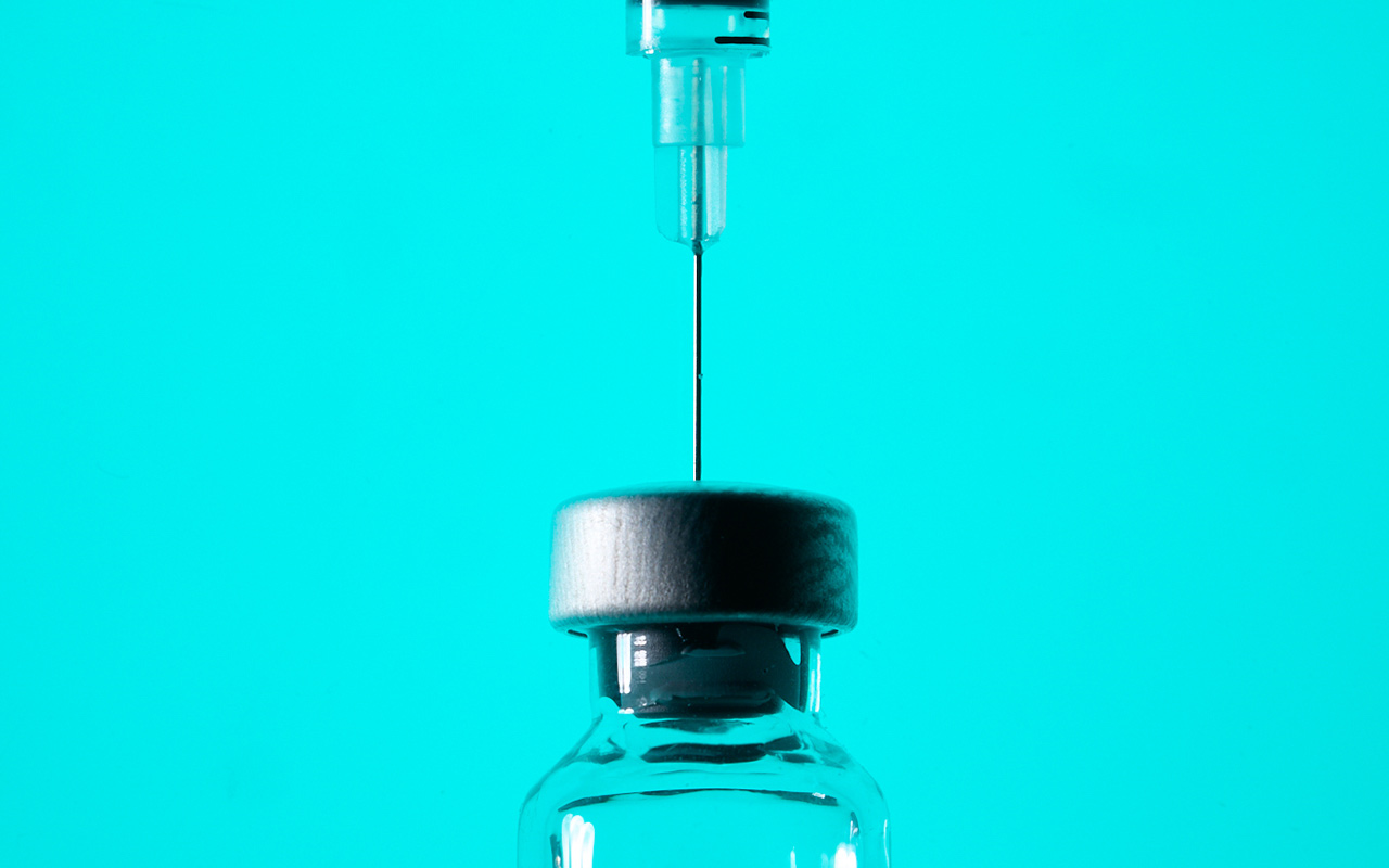 A close-up view of a needle and syringe and a glass vial, mostly in silhouette against a teal background