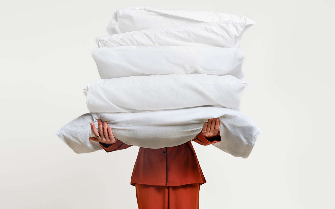 A person holds several pillows. 
