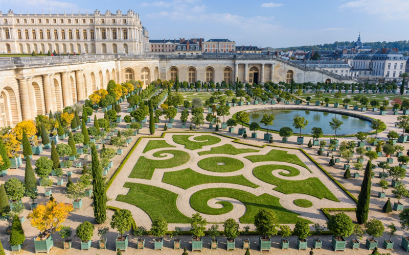 Aerial view of the gardens of Versailles. Pictures are rows and rows of trees, a winding grass garden and a large pond.