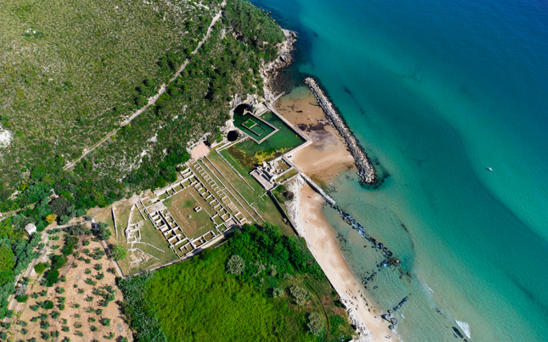 An aerial view of the Sperlonga site shows the ruins of Tiberius’s villa, the grotto mouth, and the pool cut into the beach. 