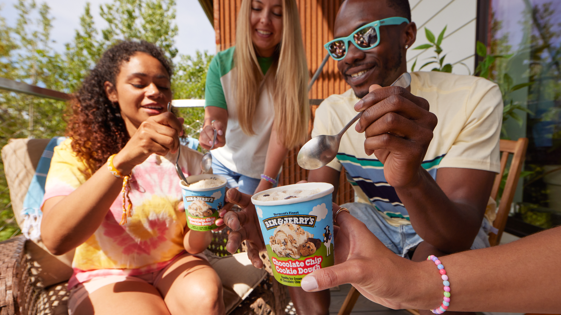 Friends sharing a pint of Ben & Jerry's Chocolate Chip Cookie Dough ice cream in a summer setting.