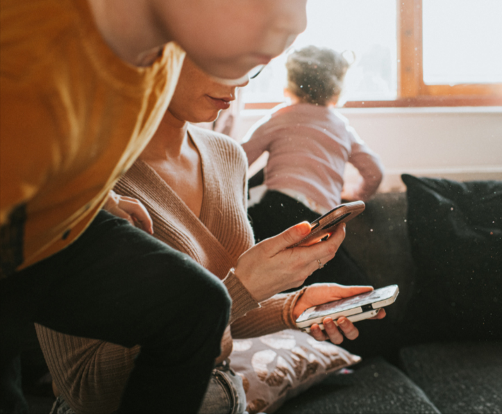 A parent juggles two phones while kids juggle in the background.