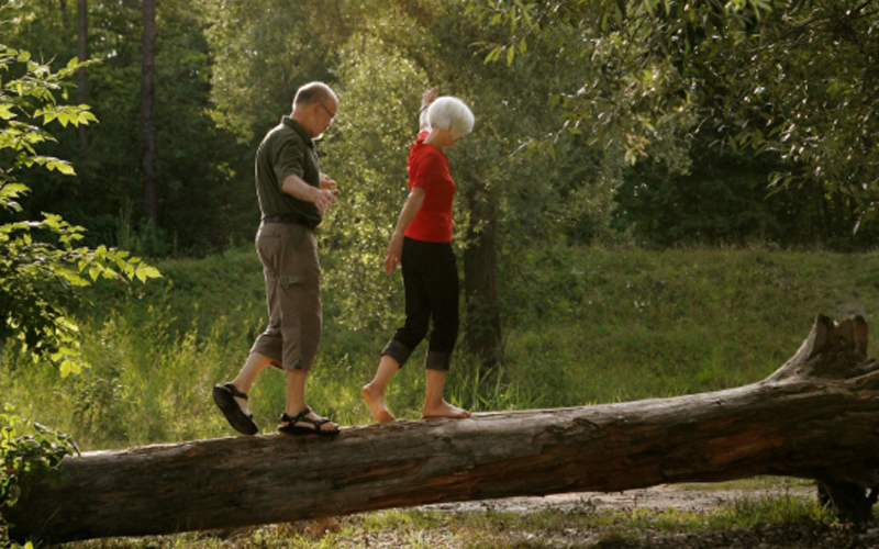 A couple balances on a log in nature.