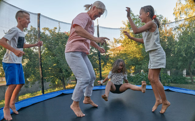 An adult and three kids jump on a trampoline.  