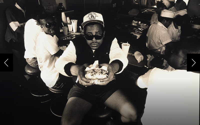 Rapper and musician Tone Loc stretches his arms toward camera, offering a half-eaten hamburger in Los Angeles in 1990. 