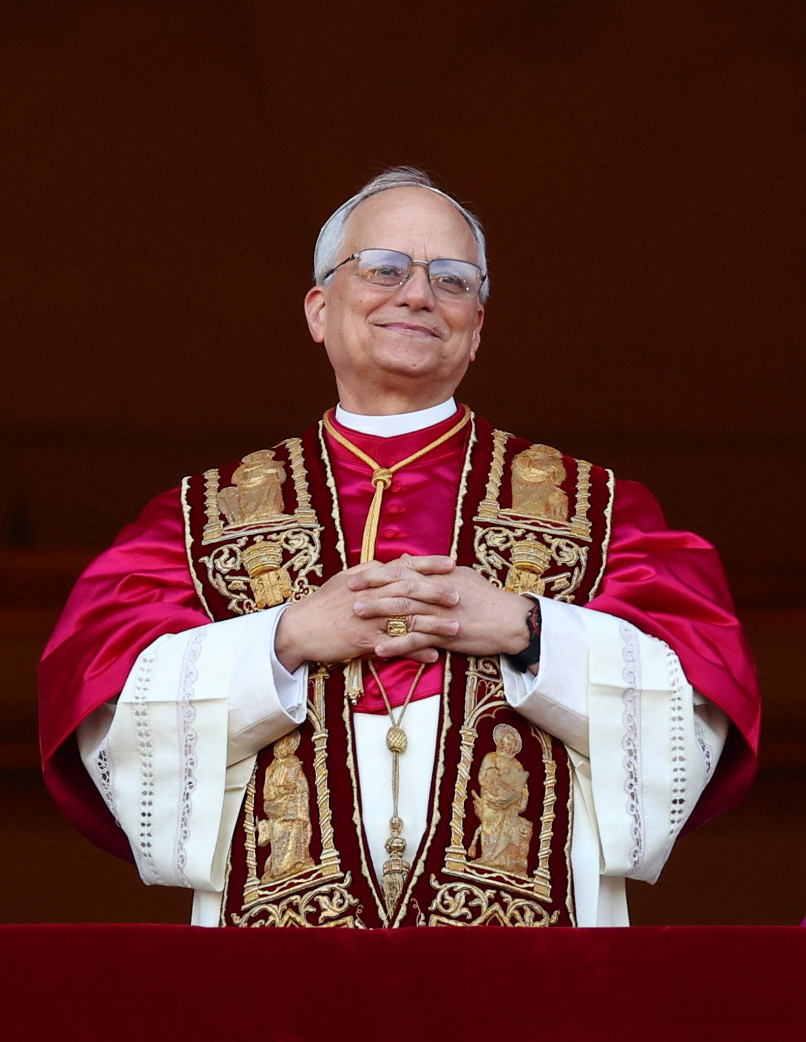 Cardinal Robert Francis Prevost folds his hands and smiles softly. He wears a red and white robe. 