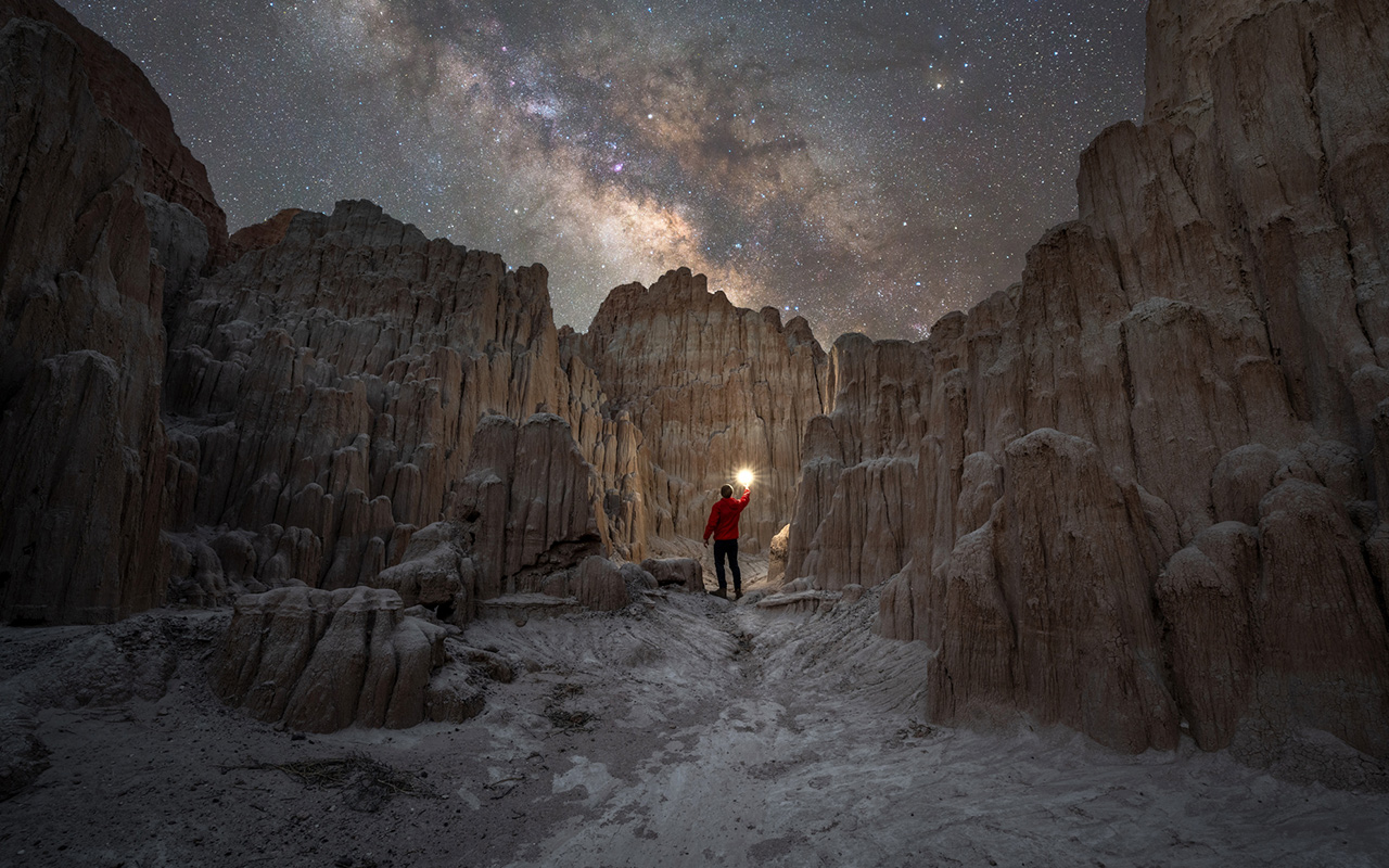 Under the Milky Way Galaxy, a night explorer stands at the entrance to Moon Caves in Nevada's Cathedral Gorge State Park. 