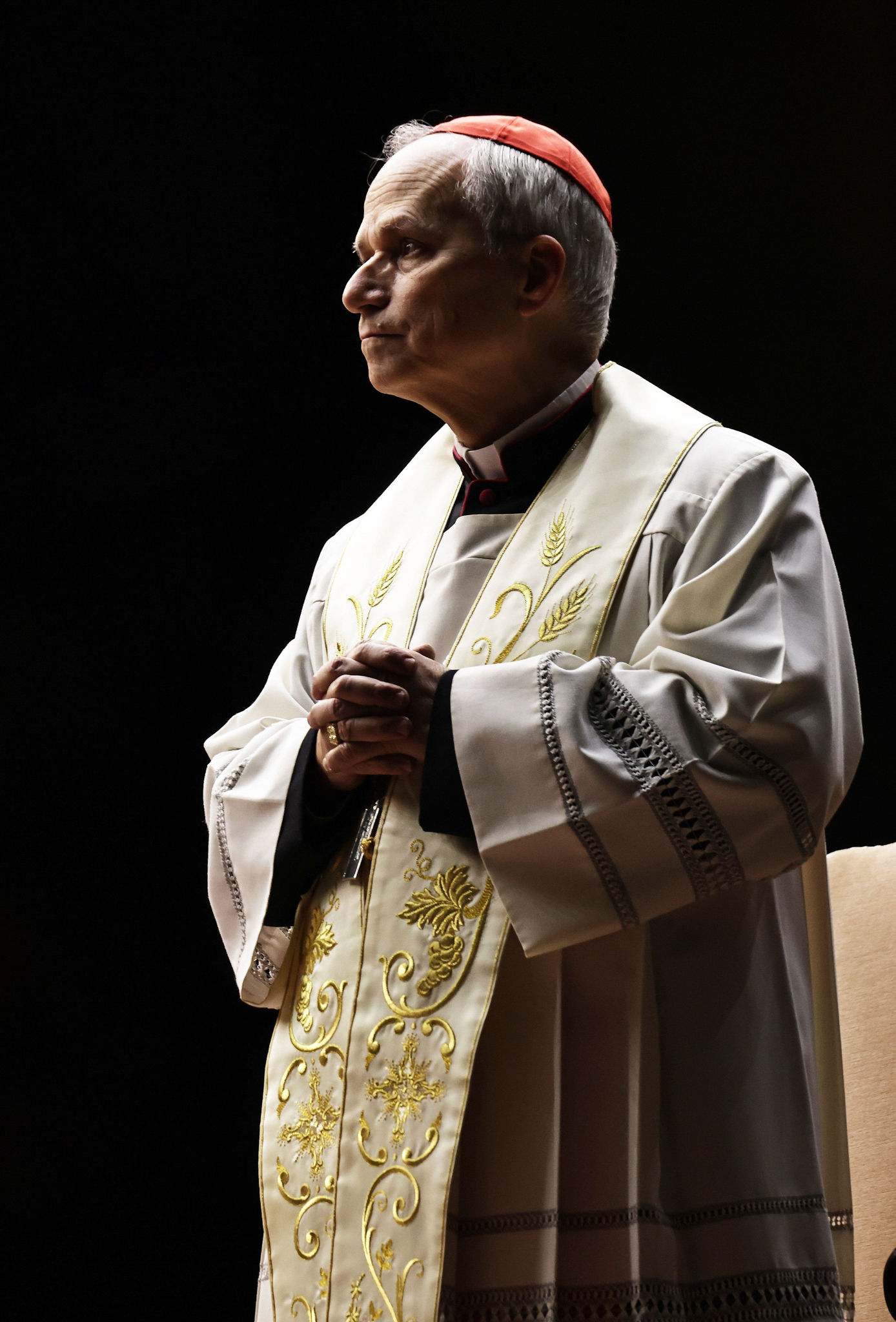 Cardinal Robert Prevost’s hands are clasped while looking outward on a black background. 