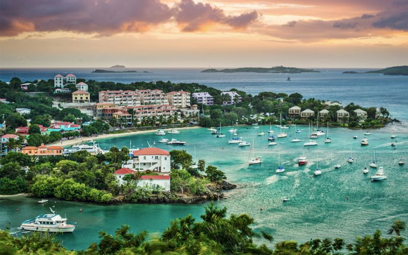 Houses line the shore of the Virgin Islands and many boats sail across light blue waters.