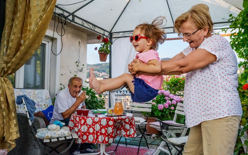 An elderly couple play with a small child in sunglasses.