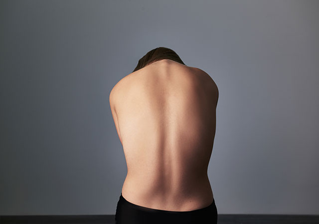 A shirtless person sits with their back towards the camera, hunched over.