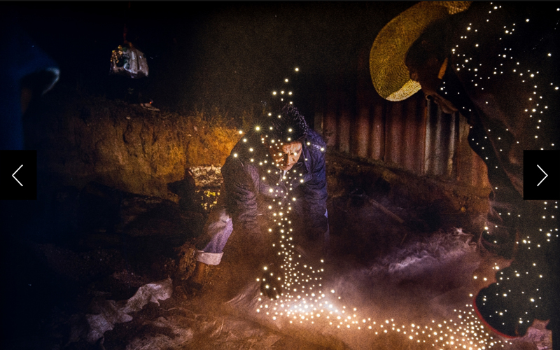 A man cooking beef in an underground oven for a shared meal is illuminated in pinpricks of light. 
