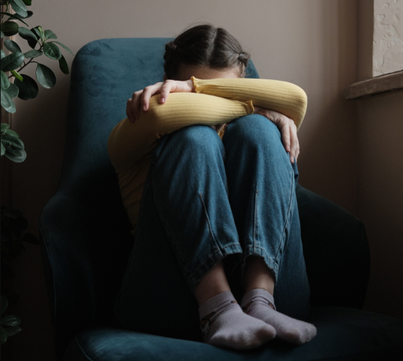 A teenager sits on a chair with her head in her arms