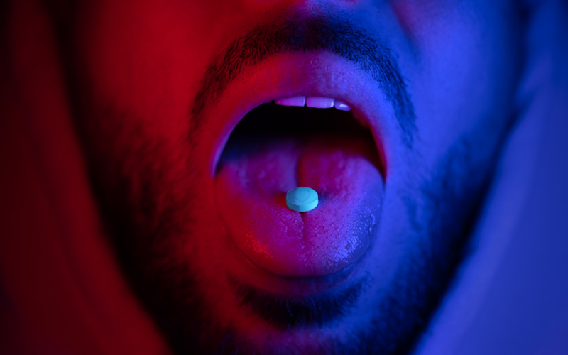 A pill rests on the tongue of a man’s open mouth
