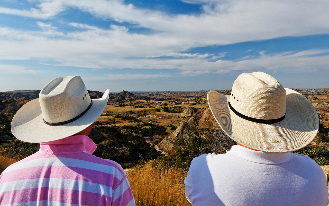 Two people with cowboy hats look out over Medora, North Dakota.