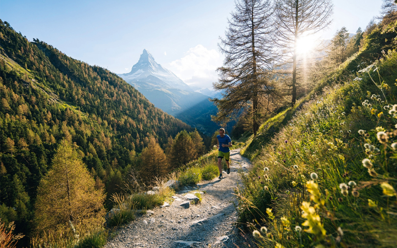 A man runs on a leafy path with a mountain in the distance.