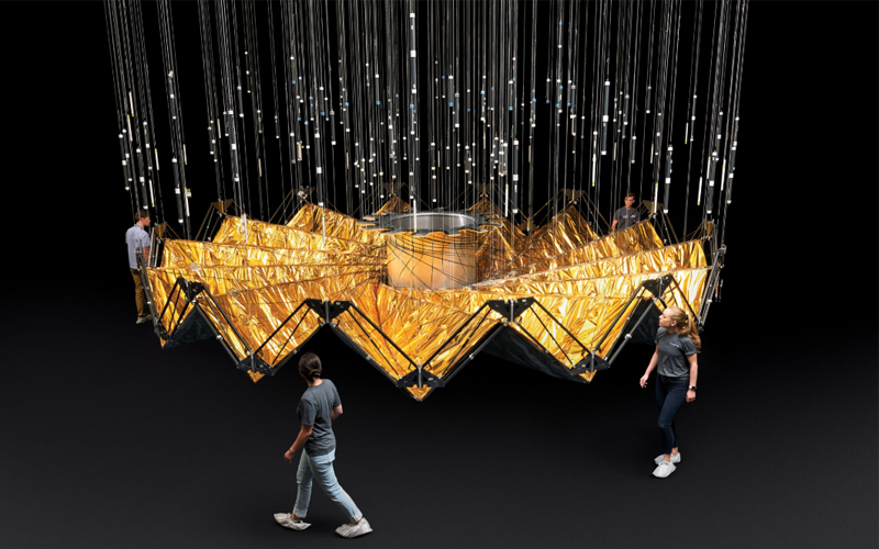 Several people circle around a half-scale prototype for a starshade, which looks like a folded golden structure. 