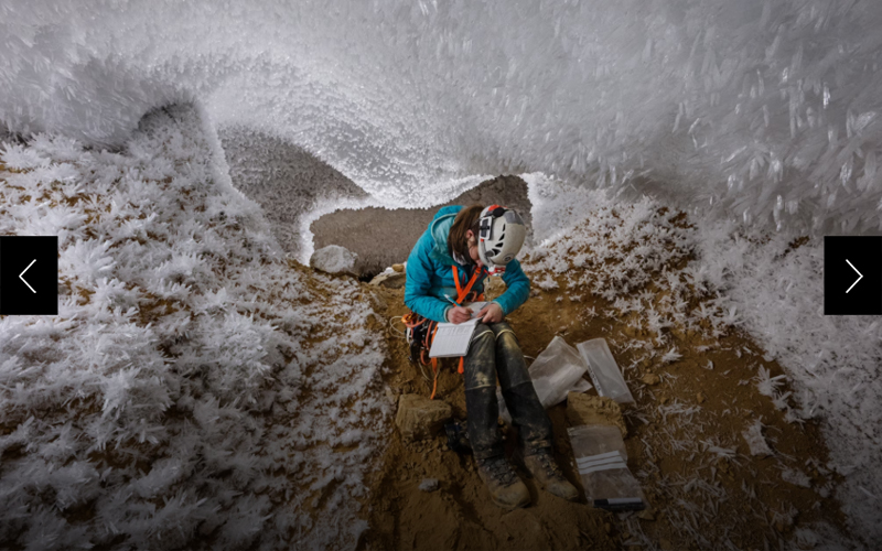Underneath a ceiling of hoarfrost crystals and ice, a woman takes notes while sitting in a cave. 