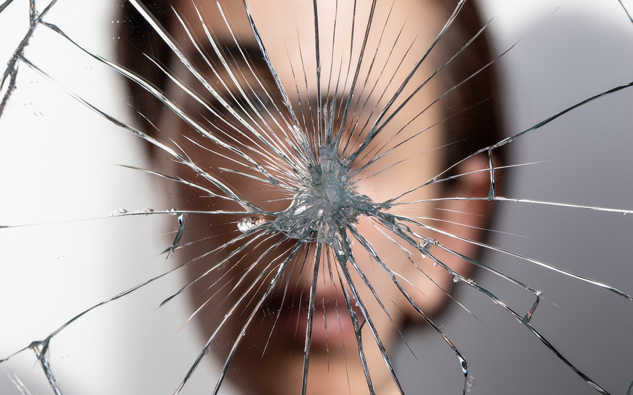 A person stares at their reflection in a shattered mirror 