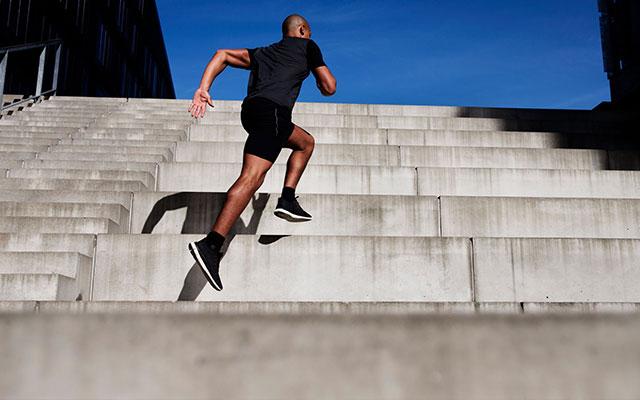 A man in black workout clothes sprint up some stairs.