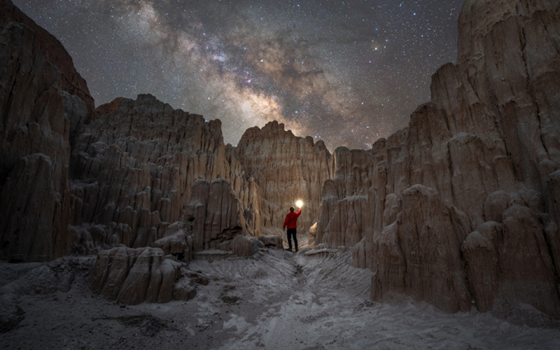 Under the Milky Way Galaxy, a night explorer stands at the entrance to Moon Caves in Nevada's Cathedral Gorge State Park.