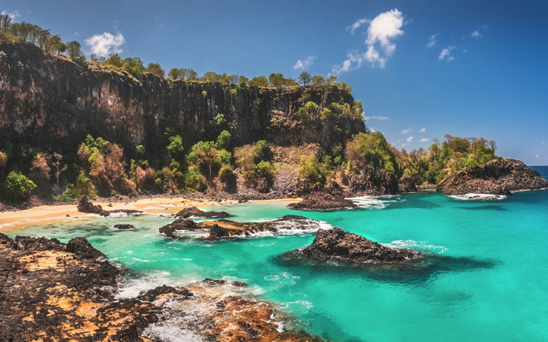 An emerald-colored beach near a tall cliffside. 