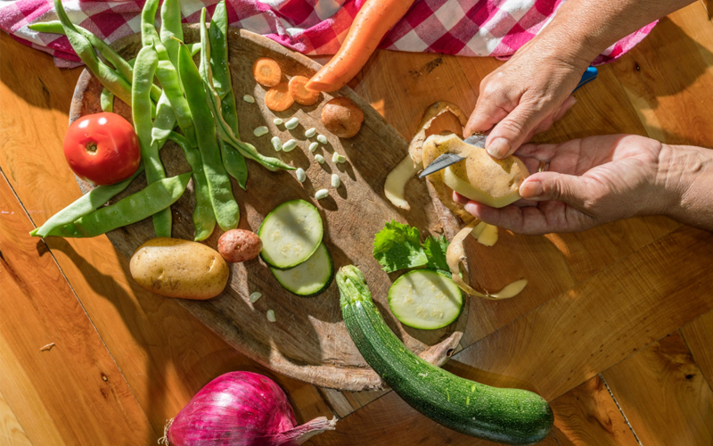 Potatoes, carrots, cucumbers, onions, and snow peas are being chopped on a counter.