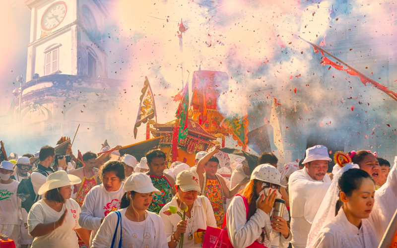 A crowd of people in white parade down the streets amid confetti and smoke. 